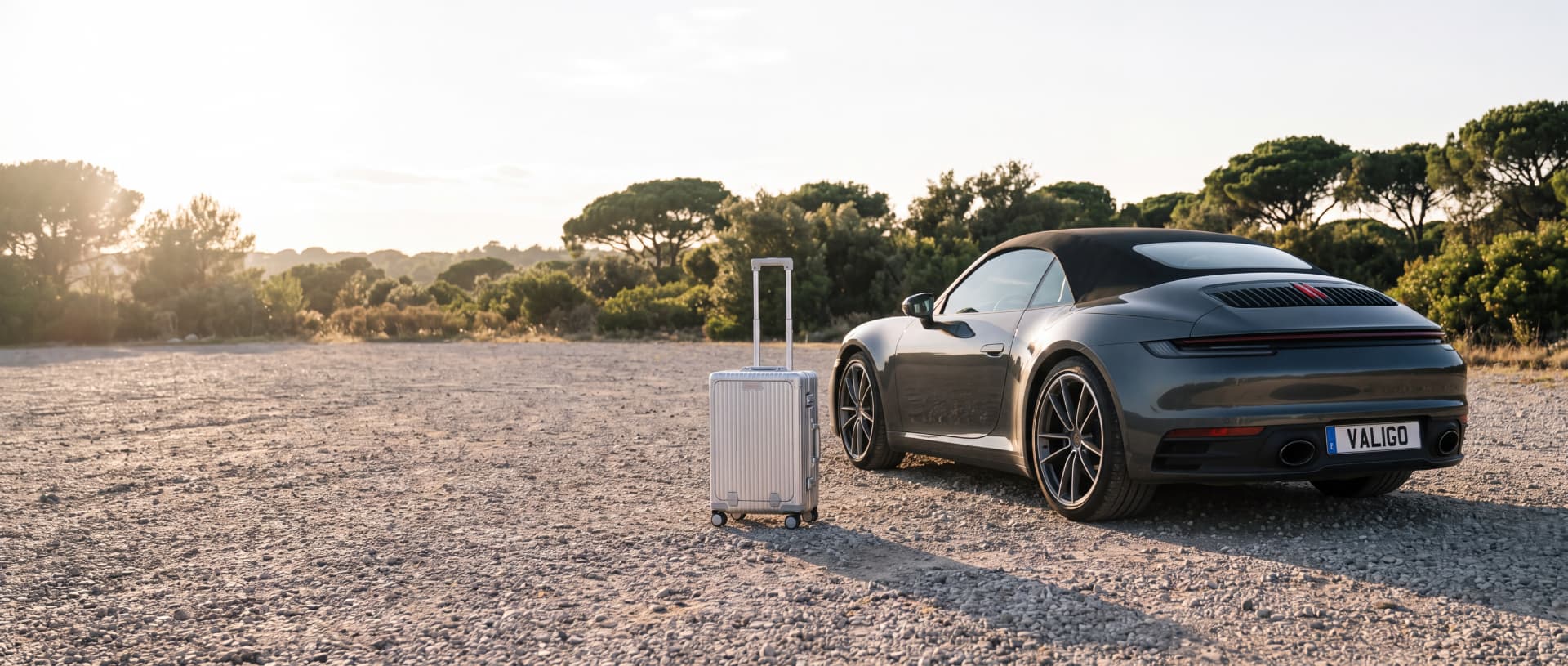 Valise cabine Valigo posée près d'un coupé sportif anthracite au coucher du soleil